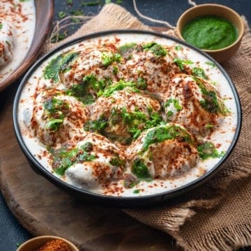 Soft fluffy Dahi Vada topped with green chutney and sweet chutney served in black plate.