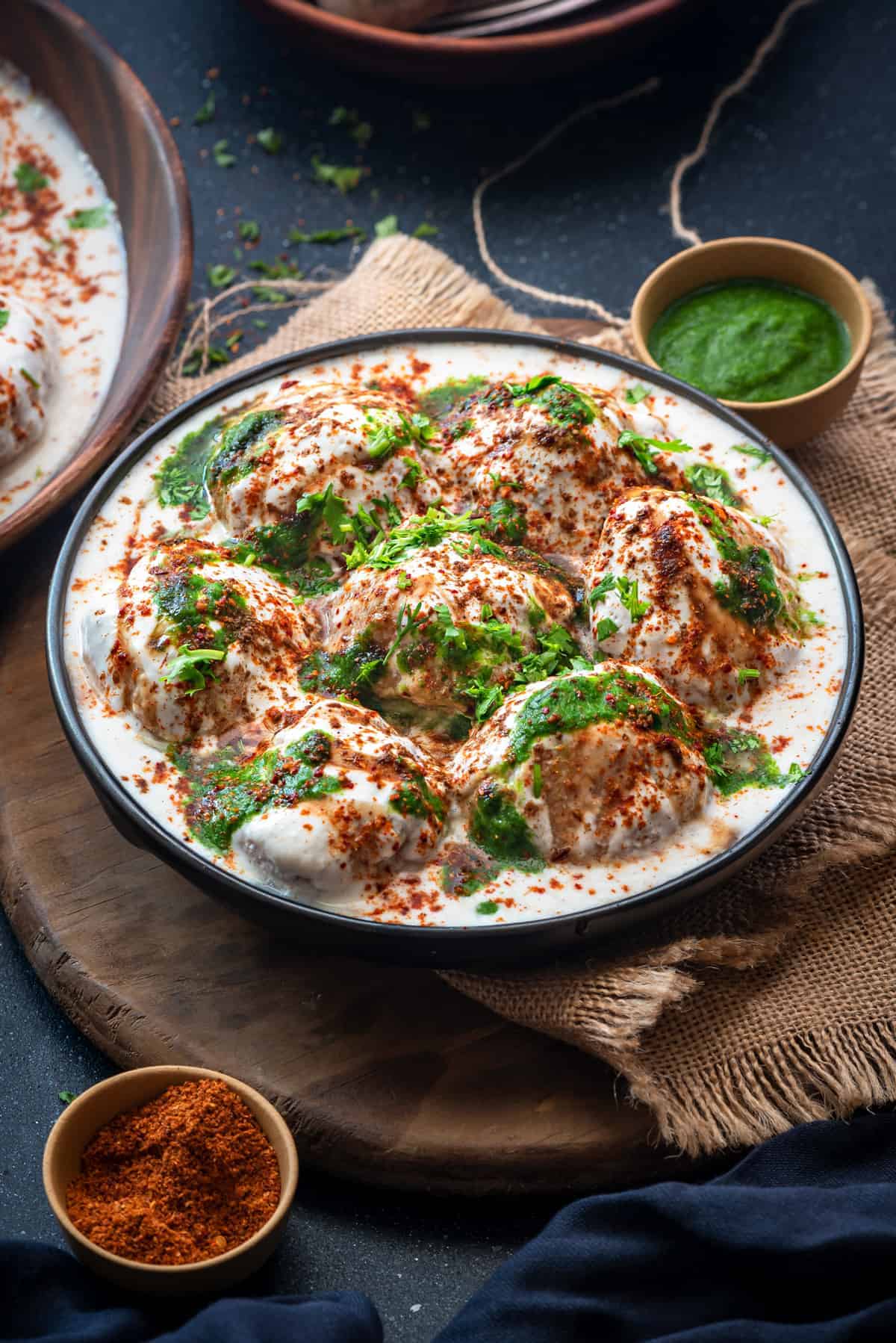 Soft fluffy Dahi Vada topped with green chutney and sweet chutney served in black plate.