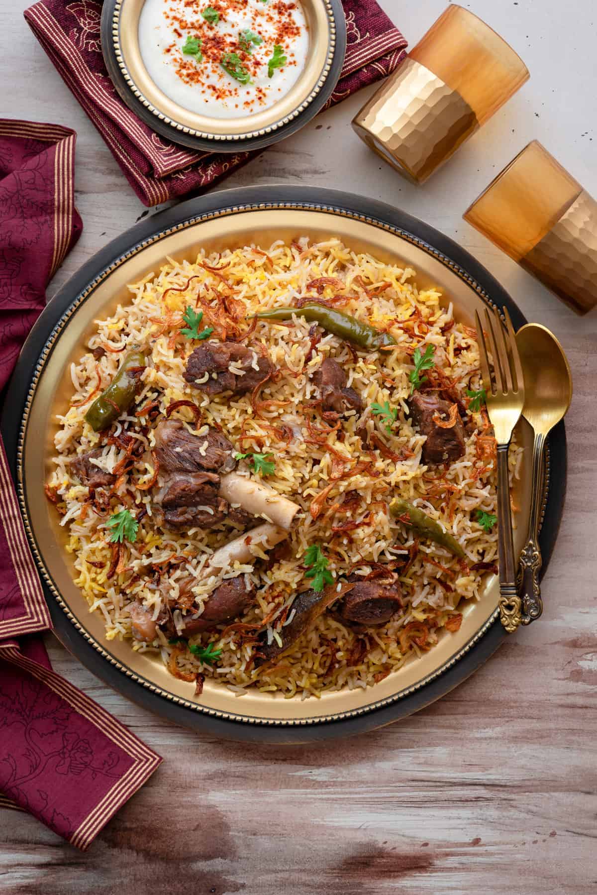 Mutton Yakhni Pulao served on traditional brass plate with raita on the side.