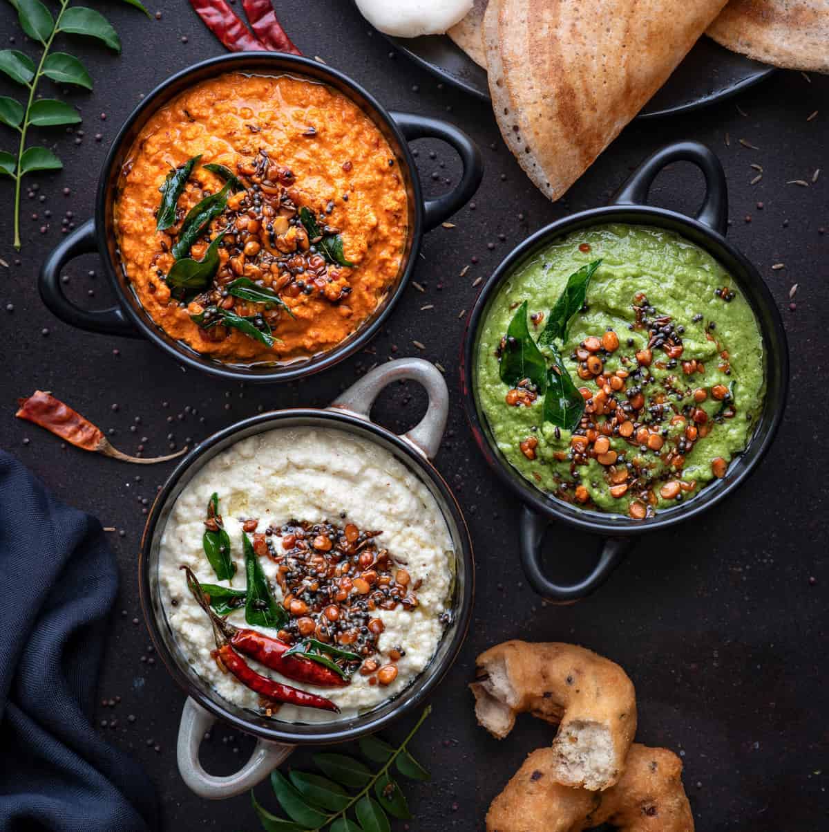 Red, white and green coconut chutney in 3 different black bowls.