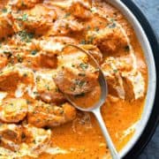 Creamy Butter Chicken curry in white bowl with spoon in it holding a chicken morsel.