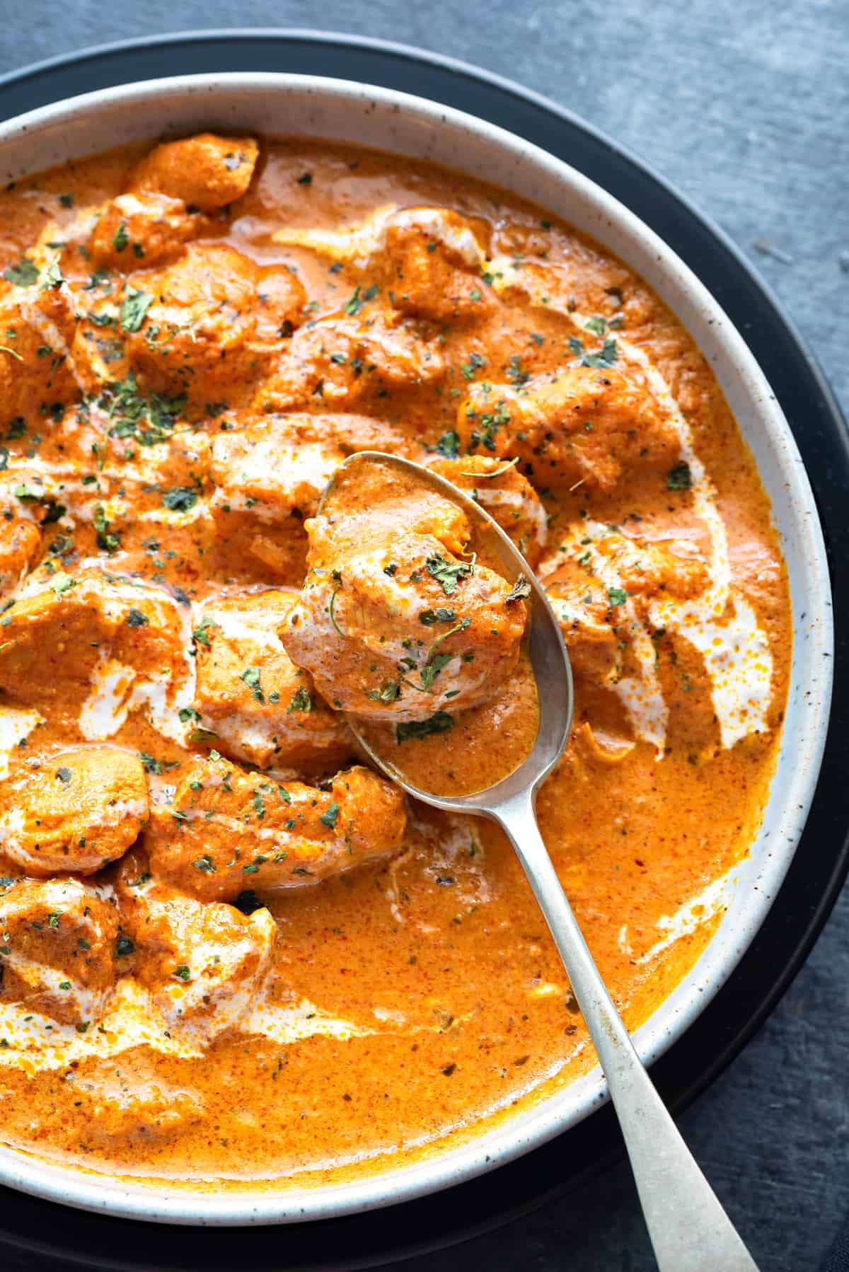 Close shot of Butter Chicken curry in a bowl with a spoon in it holding chicken morsel.