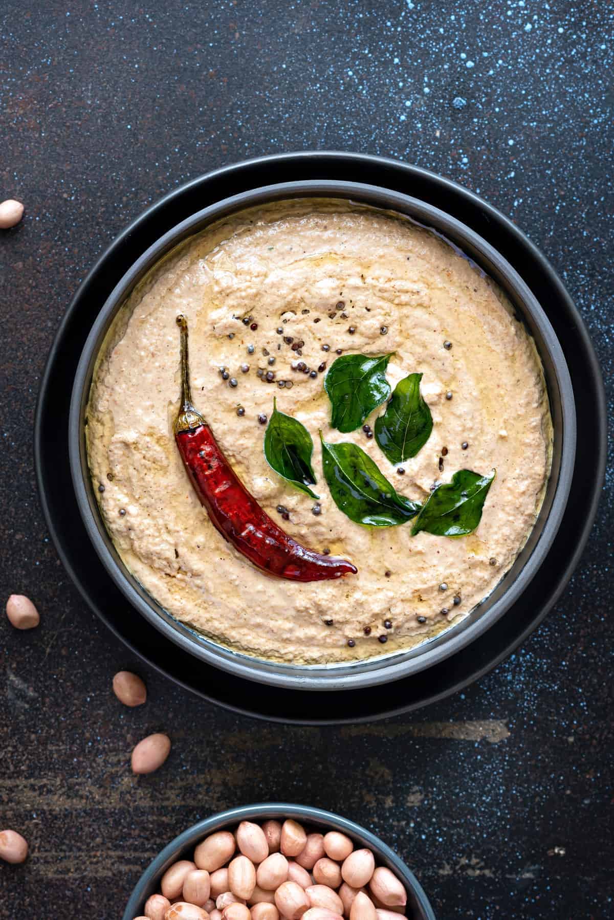 Close up shot of peanut chutney in black bowl with few groundnut seeds spread around.