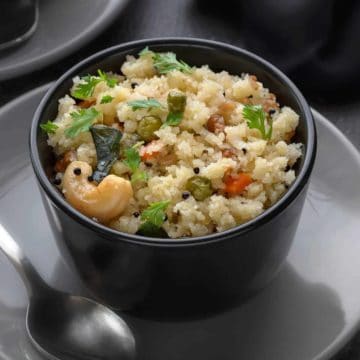 Rava Upma served in small black bowl with spoon along side.