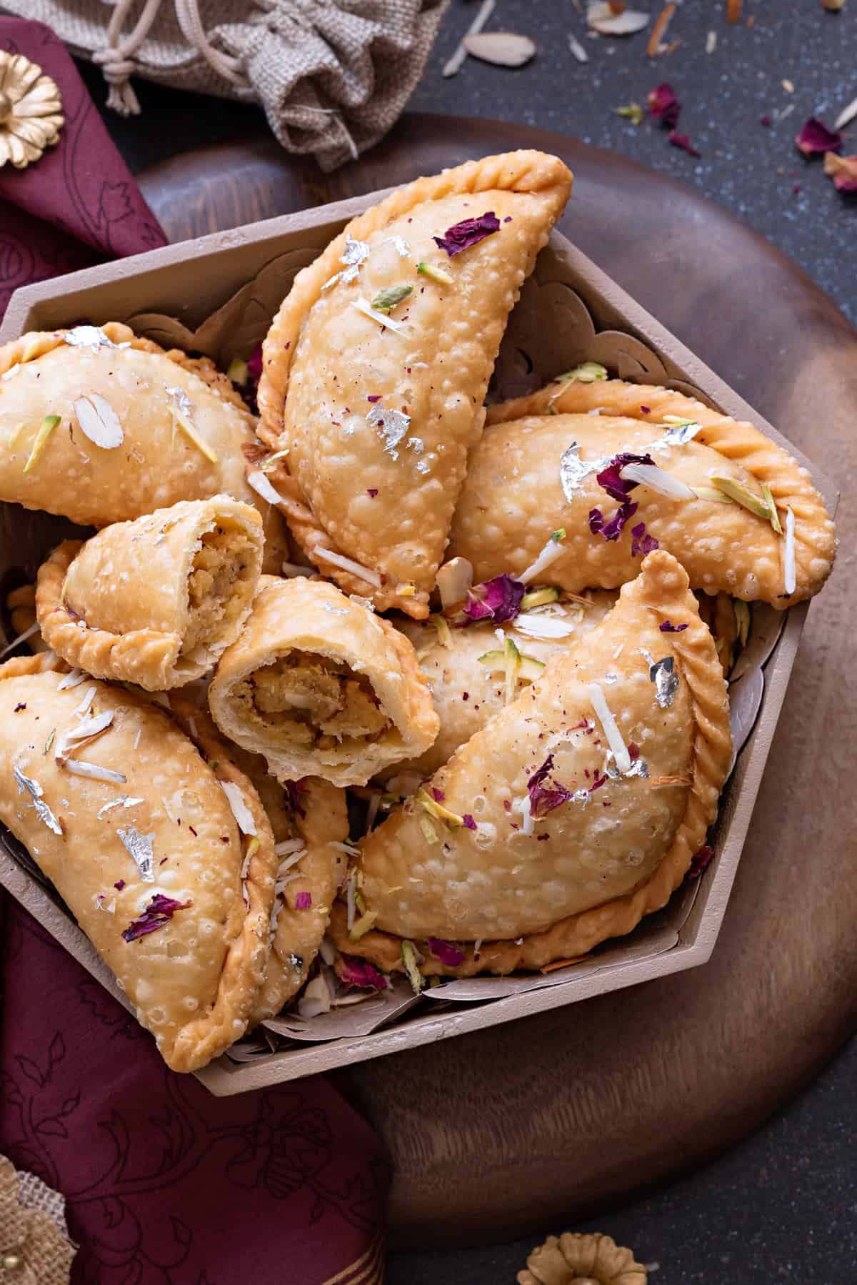 8 Gujias in a metal bowl with one cut open to show the stuffing.