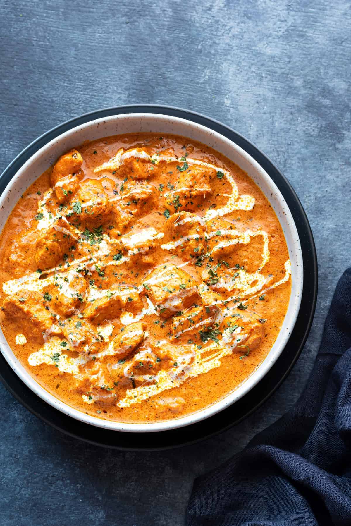 Creamy butter chicken curry served in white bowl, blue linen on side.