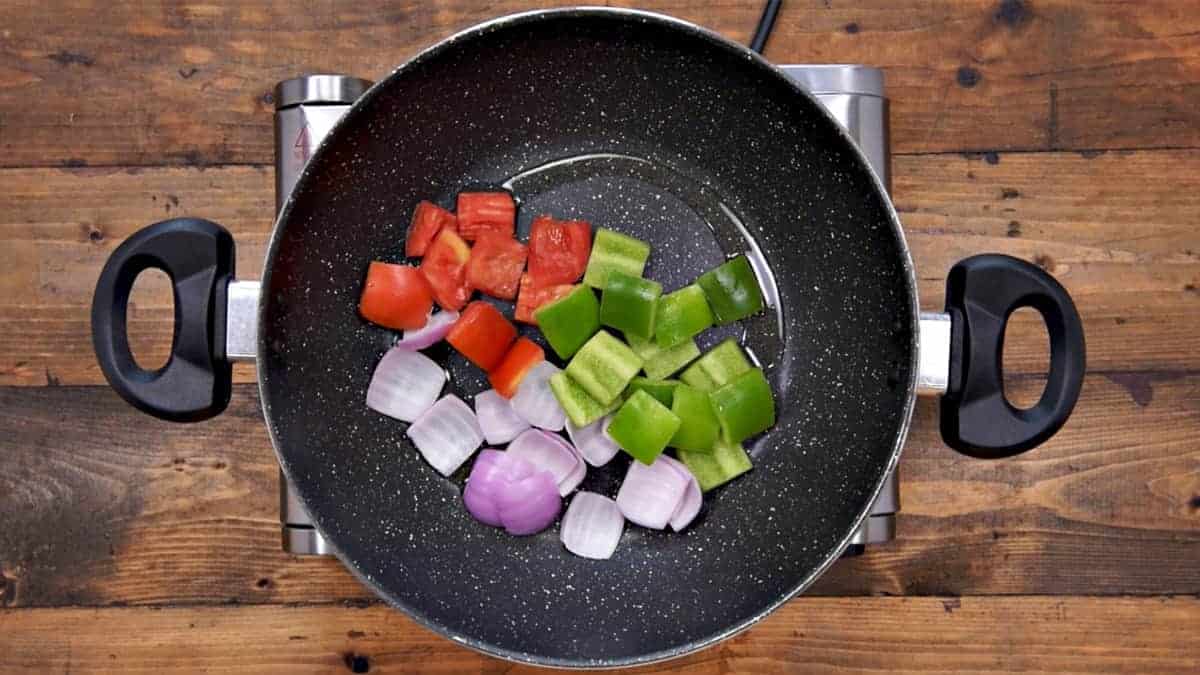 Onion, capsicum and tomato cubes added in hot oil in pan.