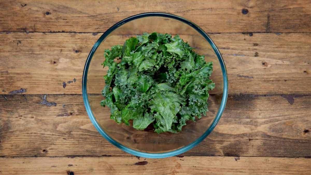 Roughly torn Kale leaves added into large glass bowl.