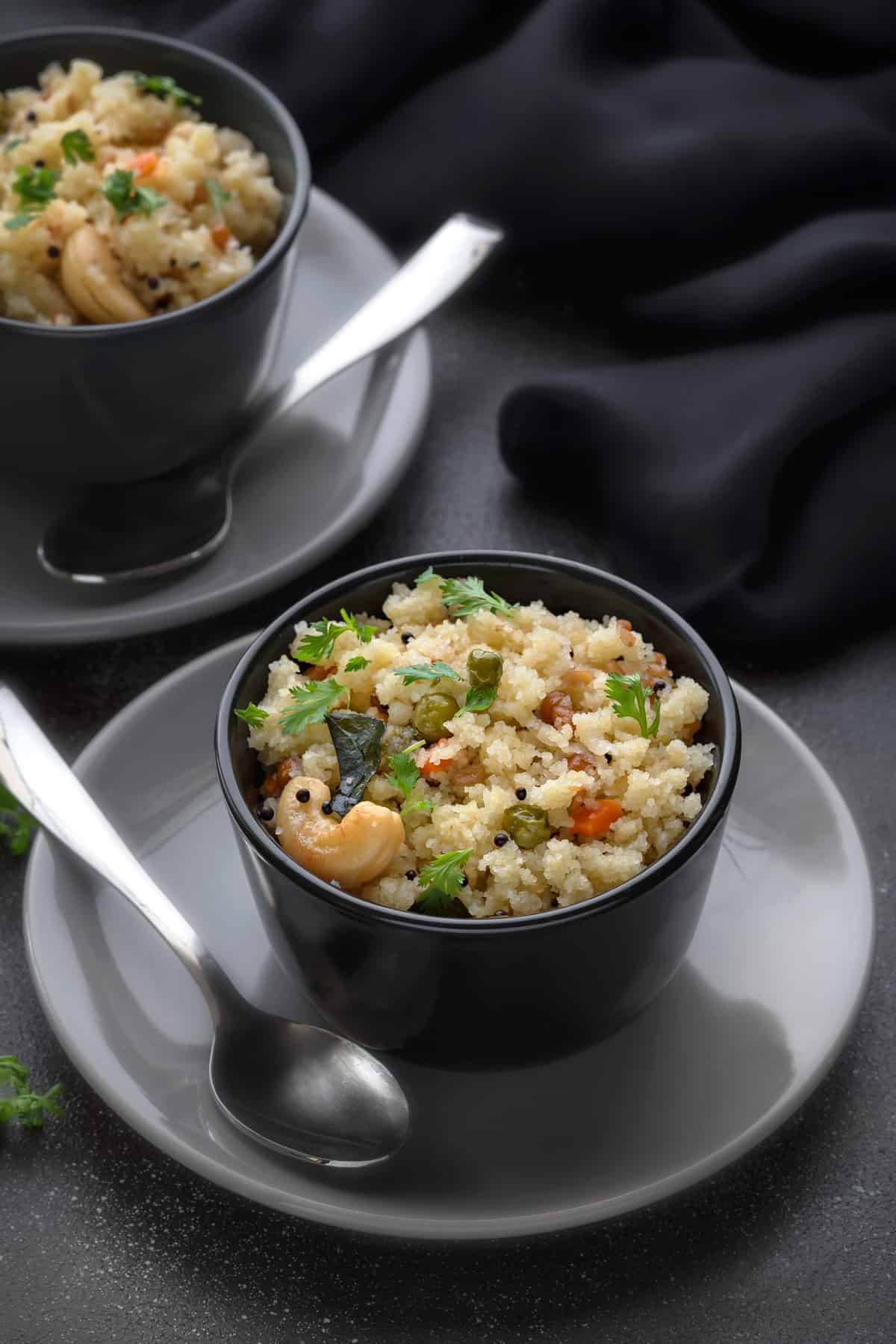 Rava Upma served in two small black bowls, with one spoon each along side.
