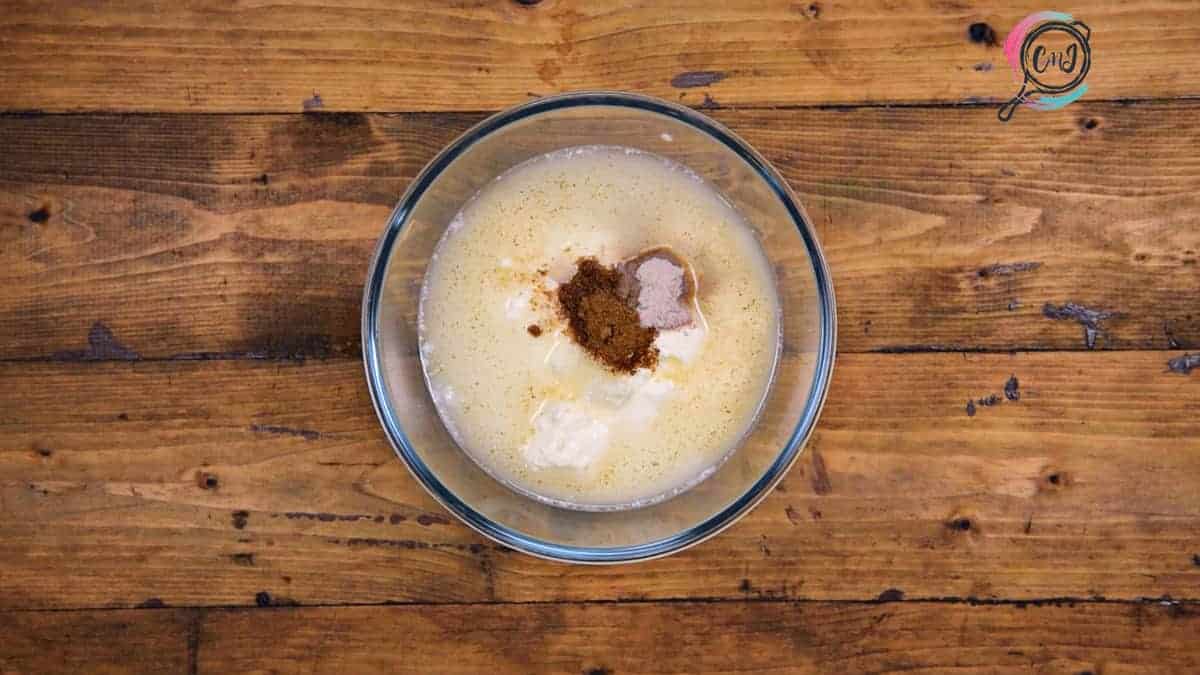 Chilled yogurt, water, cumin powder and salt added in large glass bowl.