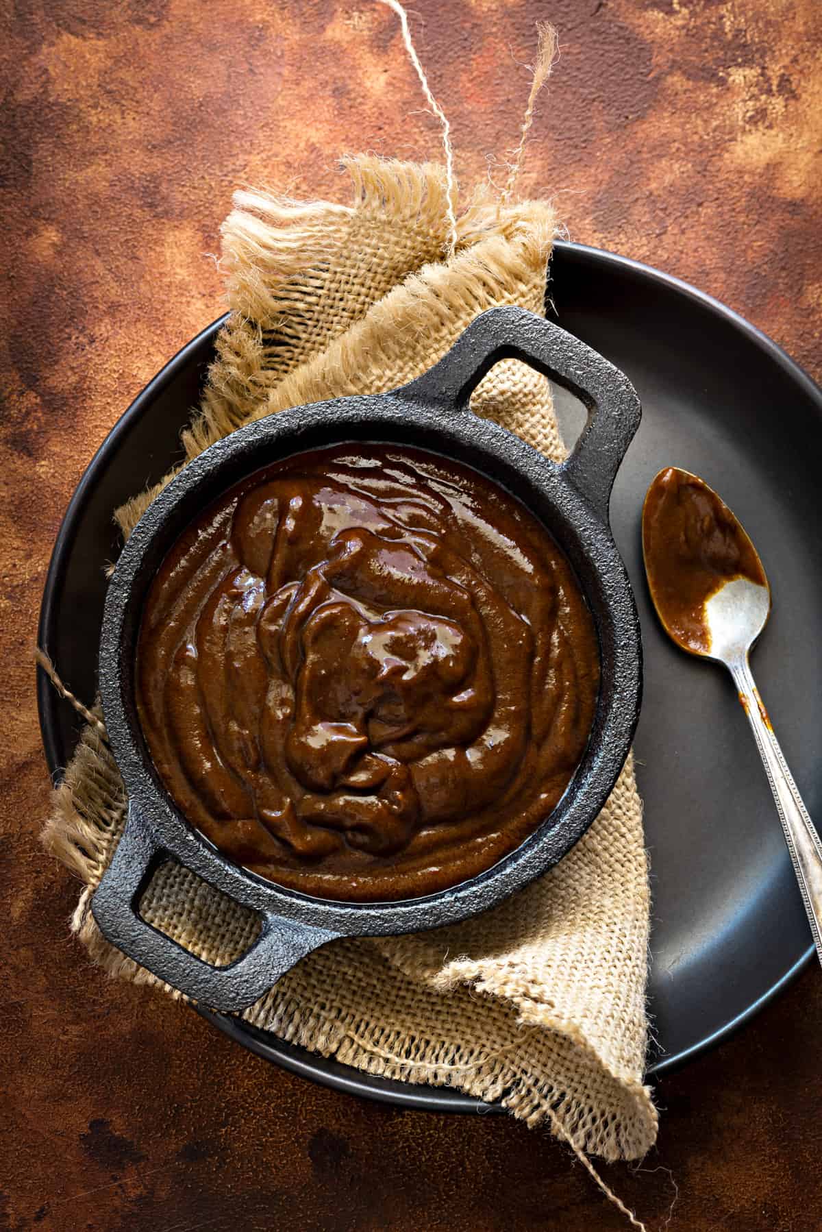 Homemade Chinese Hoisin Sauce in black bowl placed on black plate, spoon on the side.