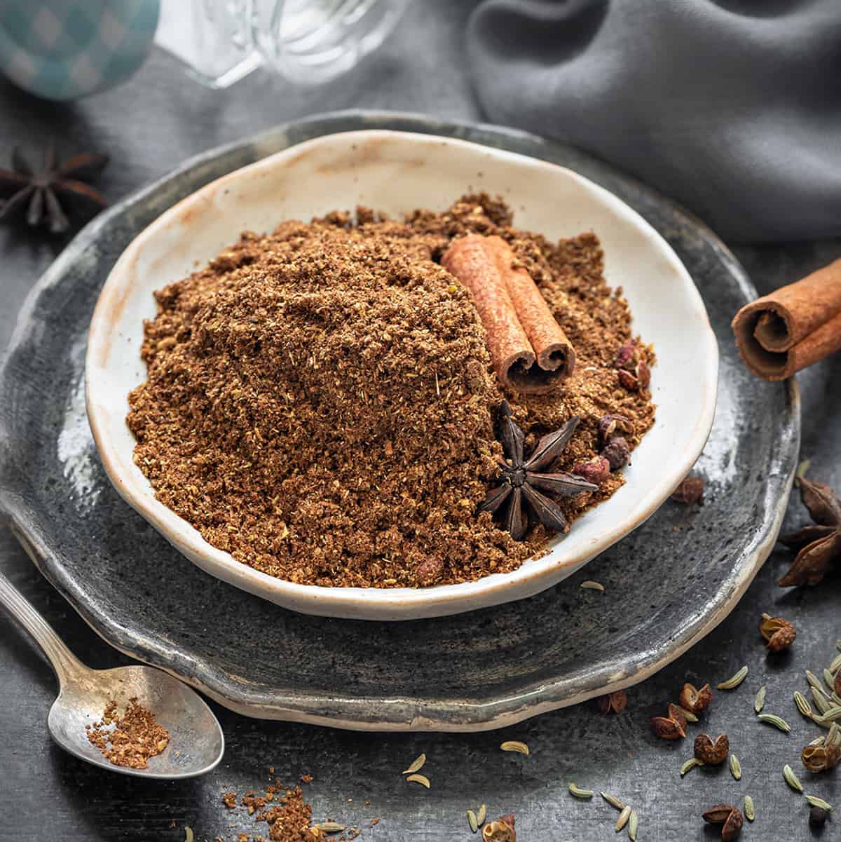 Chinese five spice powder in small ceramic plate, some whole spices spread around.