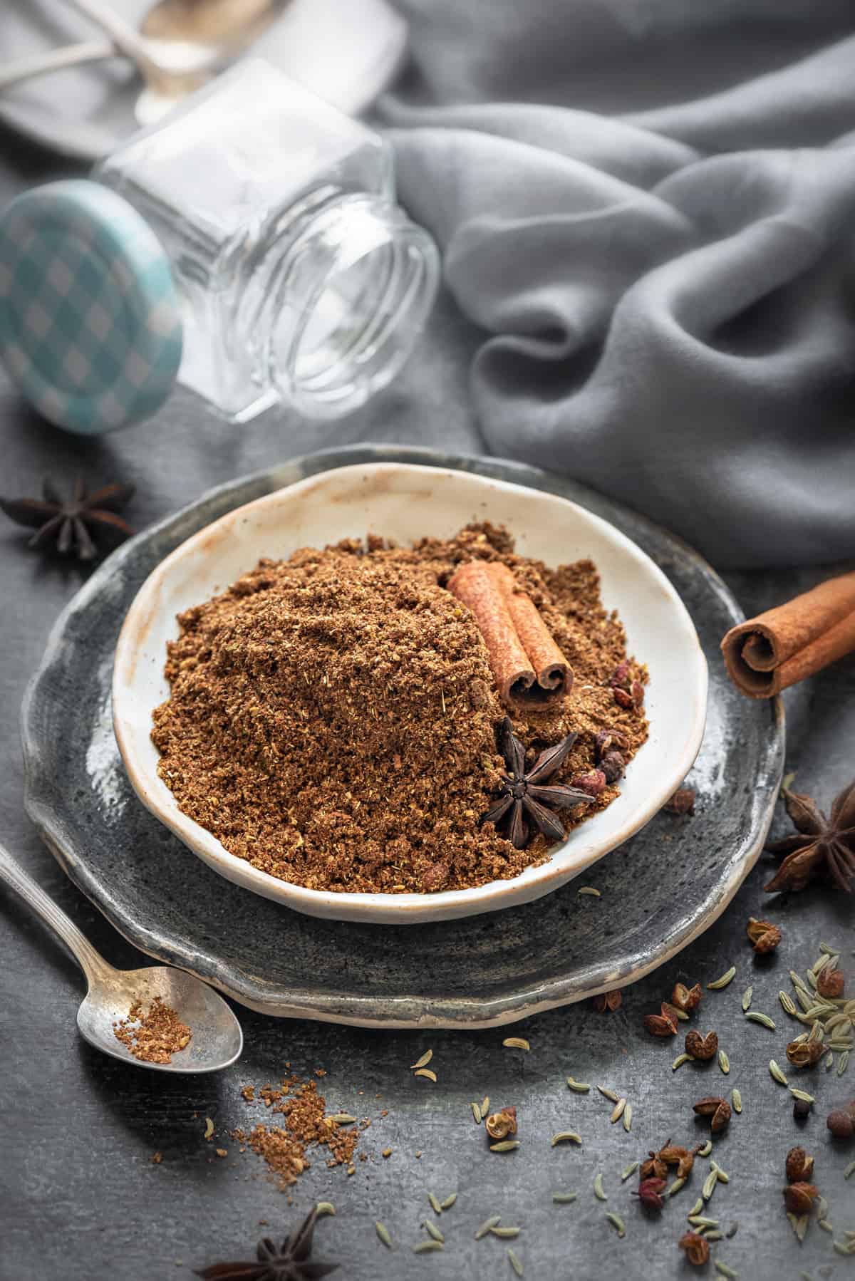 Chinese five spice powder in small ceramic plate, some whole spices spread around.