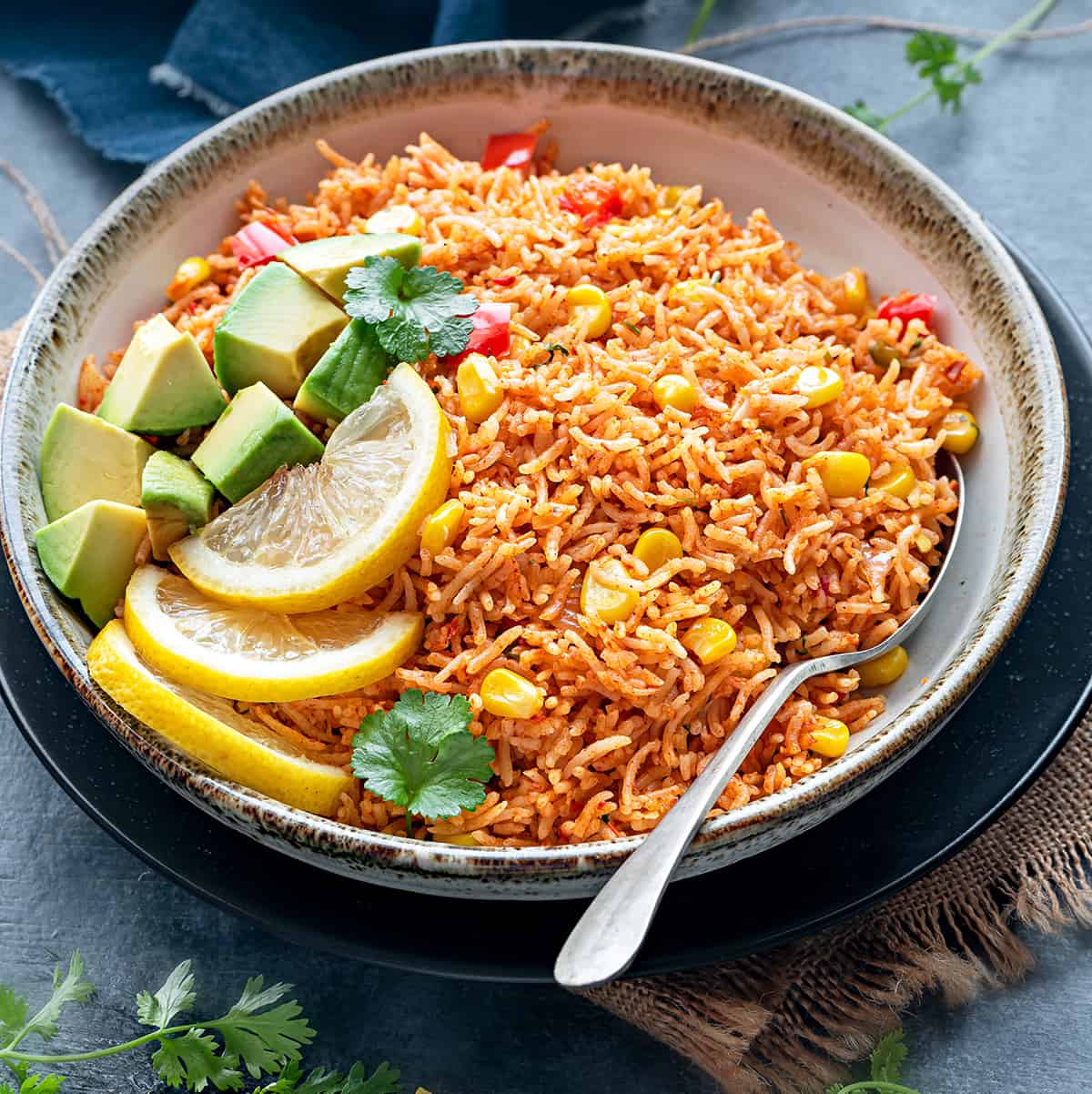 Authentic Mexican Rice topped with avocados served in grey ceramic bowl with spoon into it.