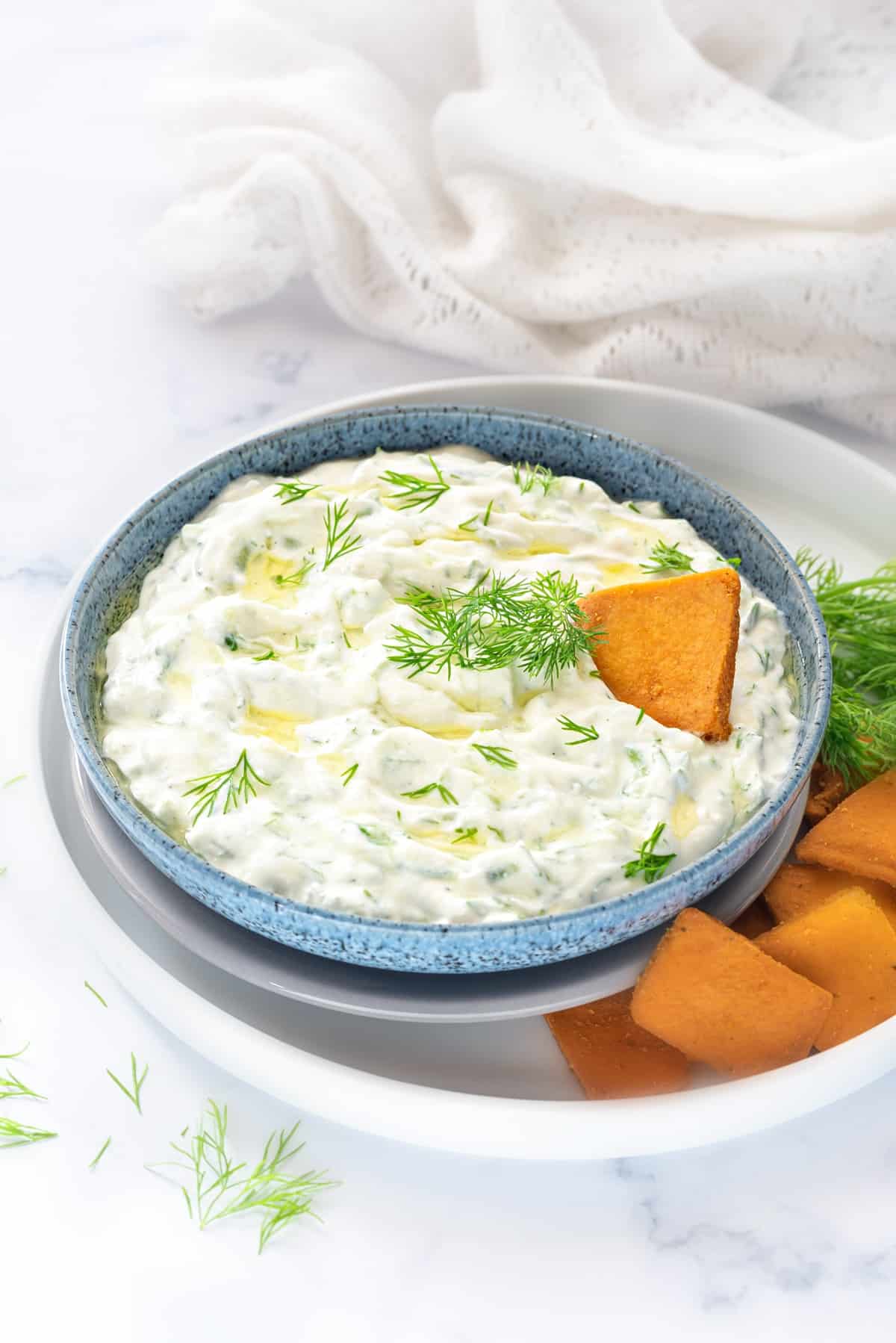 Greek Tzatziki sauce in blue bowl with some pita chips served on the side.