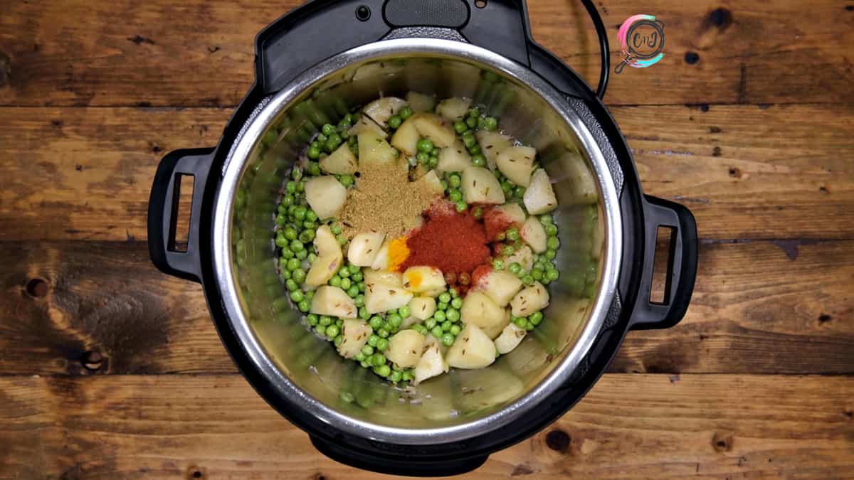 Turmeric, coriander powder and red chilli powder added to sautéed peas and potato in pot.