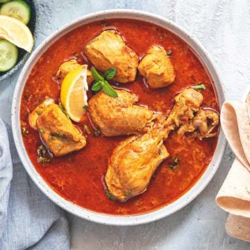 Chicken Curry served in white bowl with bread and salad on side.