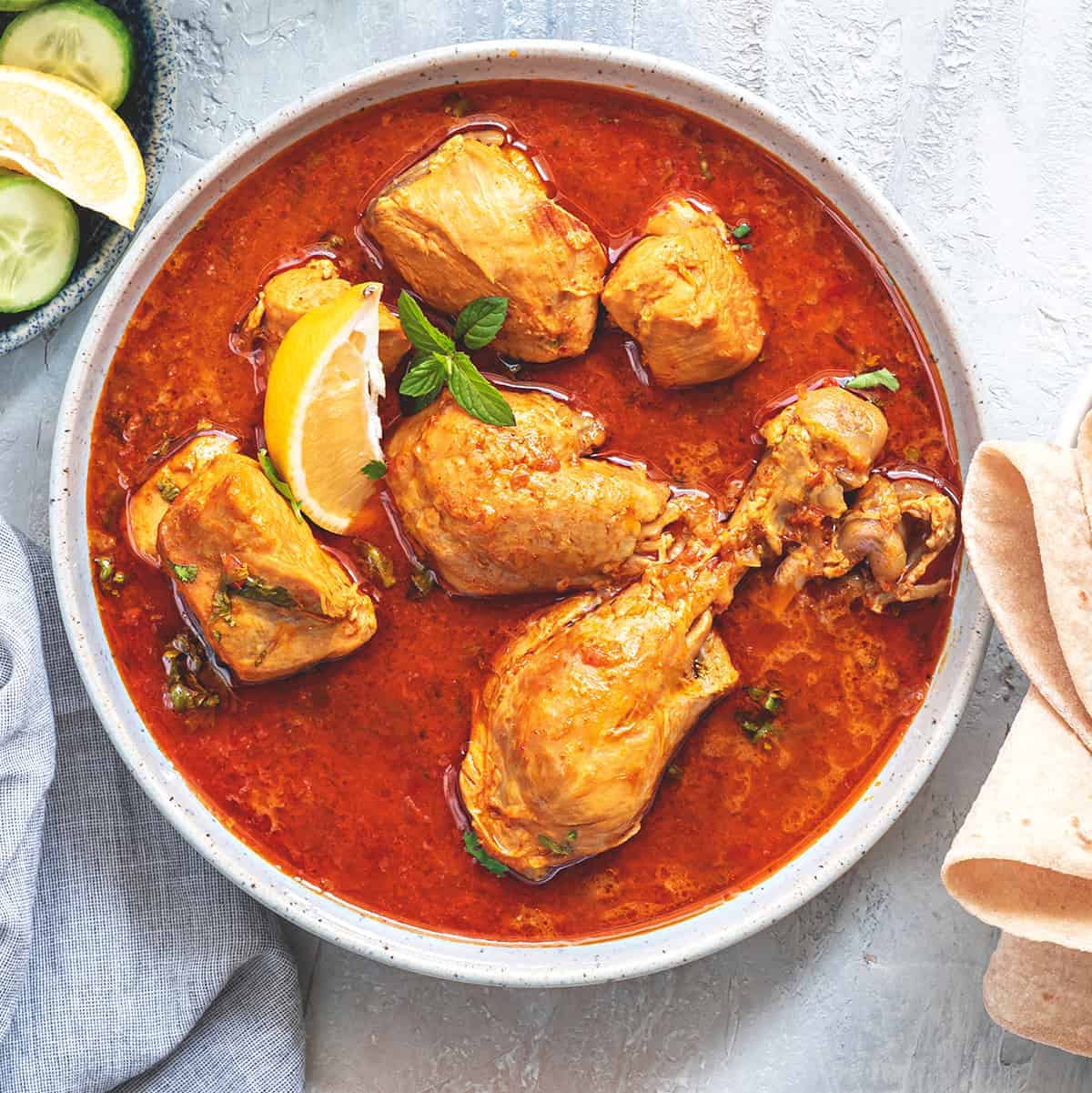 Chicken Curry served in white bowl with bread and salad on side.