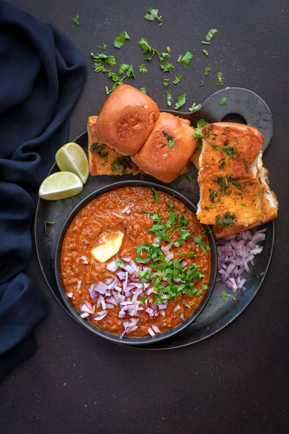 Pav bhaji served in black plate with toasted pav, lemon wedges and chopped onions.