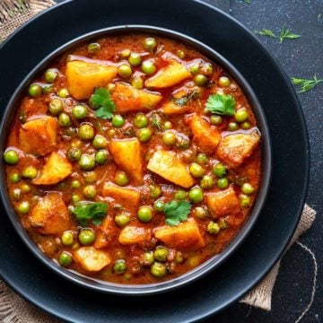 Aloo Matar curry served in black ceramic plate with some dill leaves spread around.