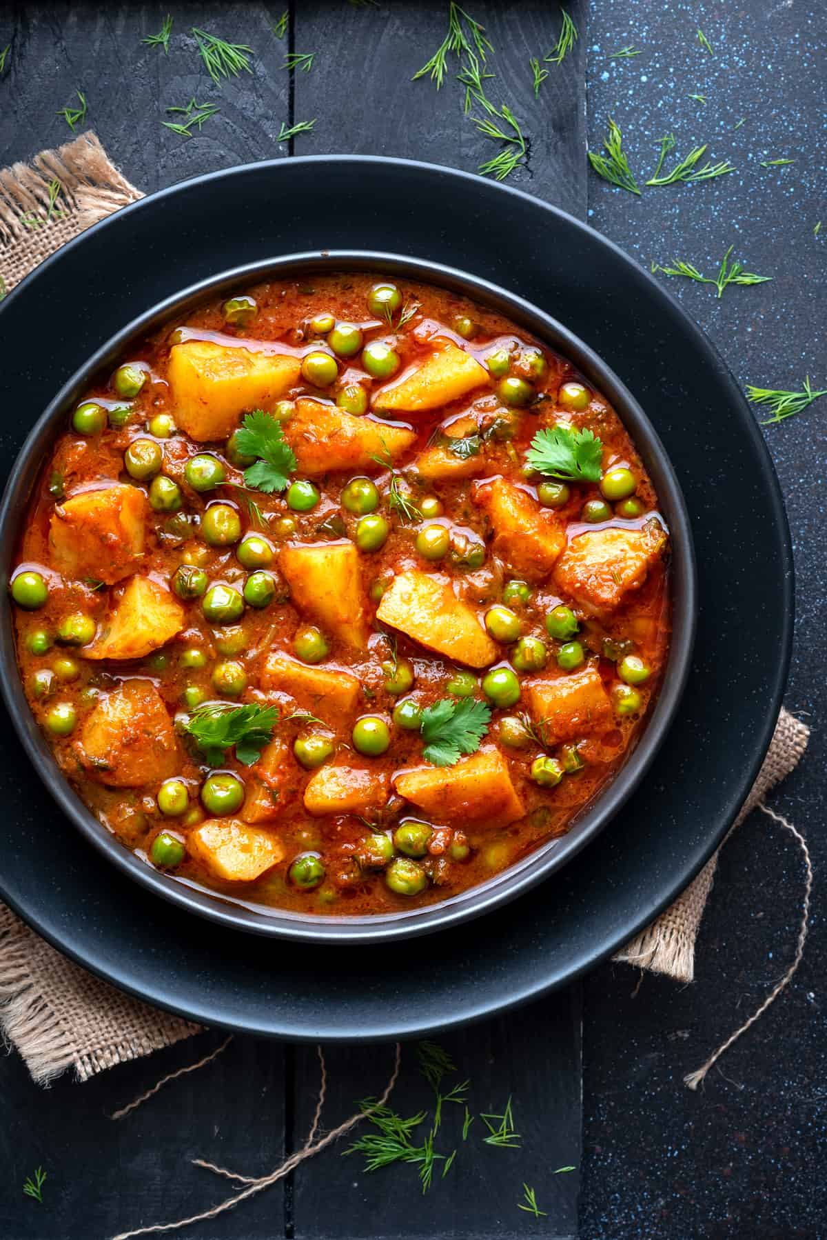 Close up shot of Aloo Matar Curryurry served in black ceramic plate.