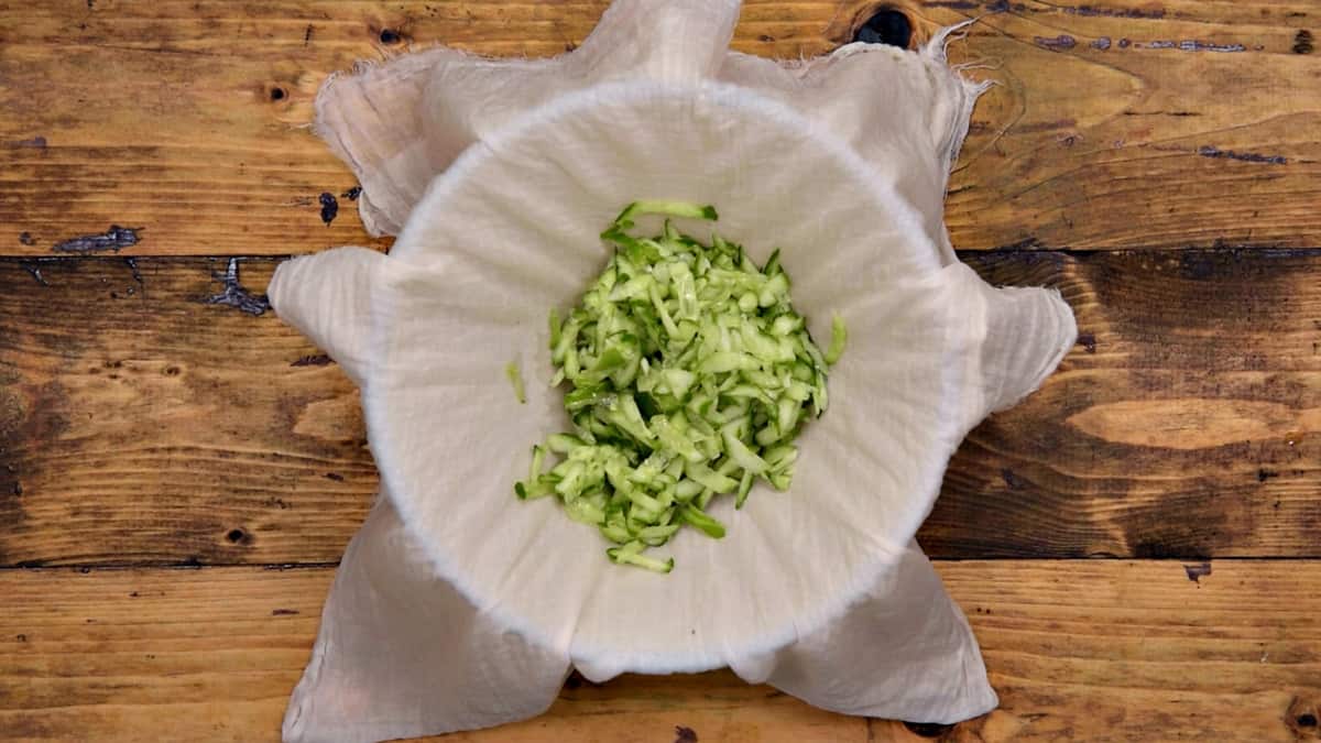 Grated English cucumber put in muslin cloth over the glass bowl to squeeze its water.