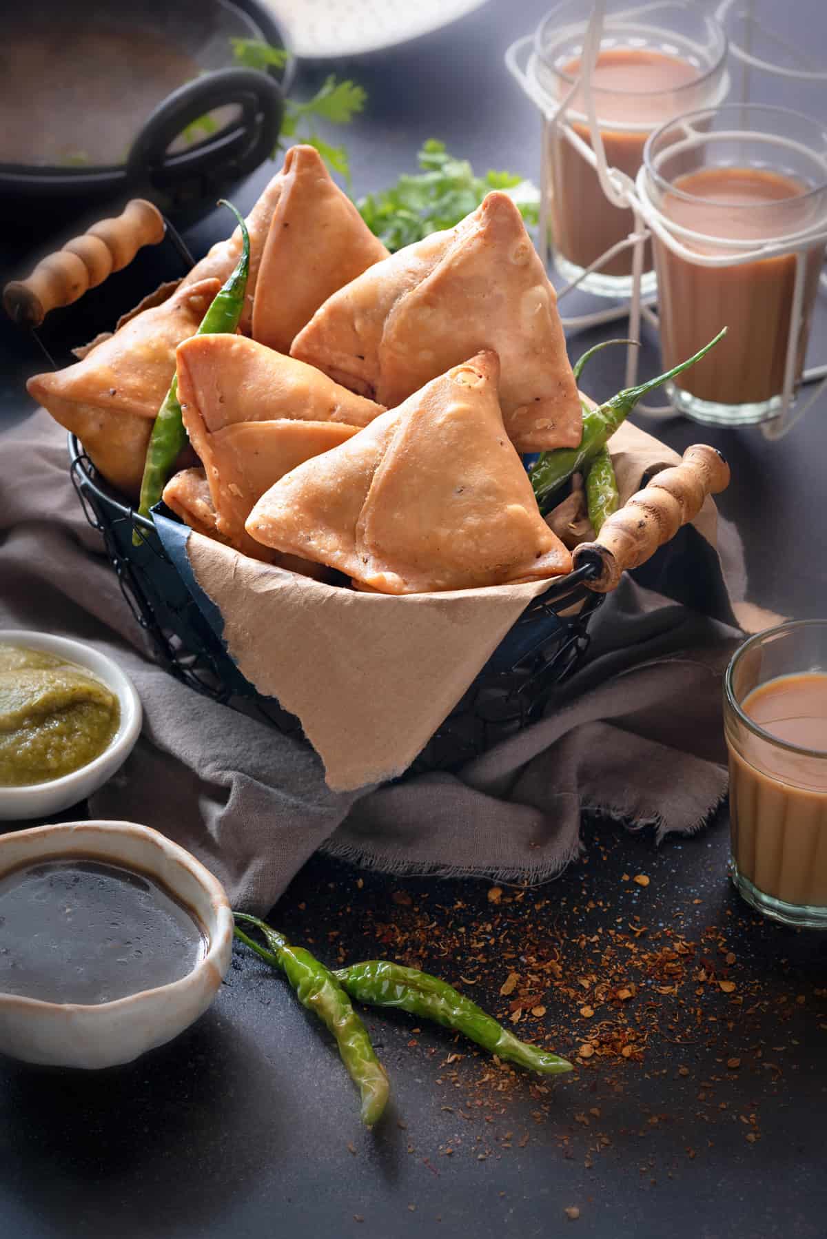 Punjabi samosas in basket, with sweet and spicy chutney, fried chilies and tea on the side.