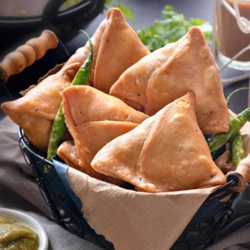 Indian Punjabi samosas in basket, with sweet and spicy chutney, fried chilies and tea on side.