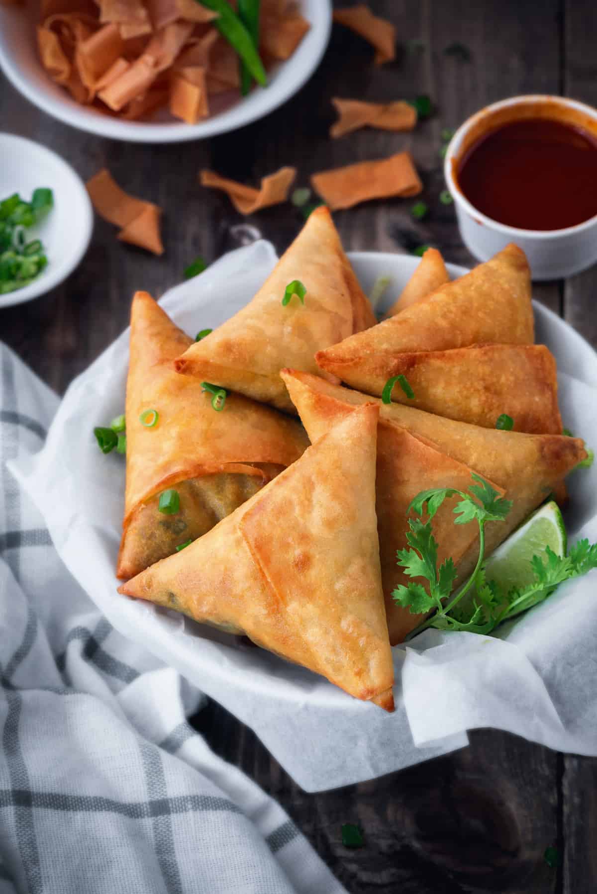 linen lined bowl filled with 5 fried keema samosa with fresh cilantro and a lime wedge