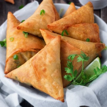 linen lined bowl filled with 5 fried keema samosa with fresh cilantro and a lime wedge