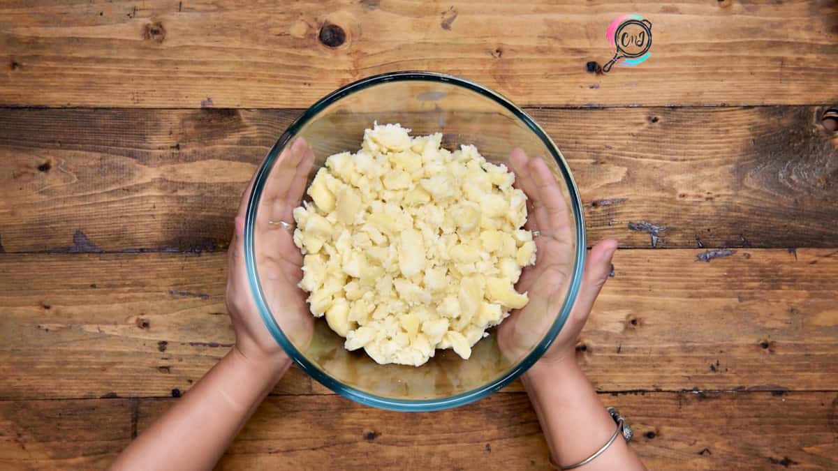 Hands holding a glass bowl having boiled and mashed potatoes in it.