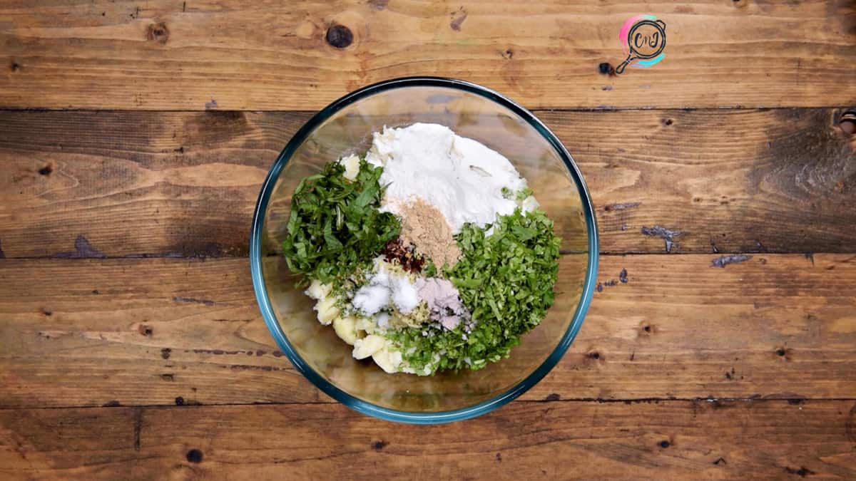 Rice flour, chopped cilantro, mint and spice powders added to the boiled potatoes in bowl.