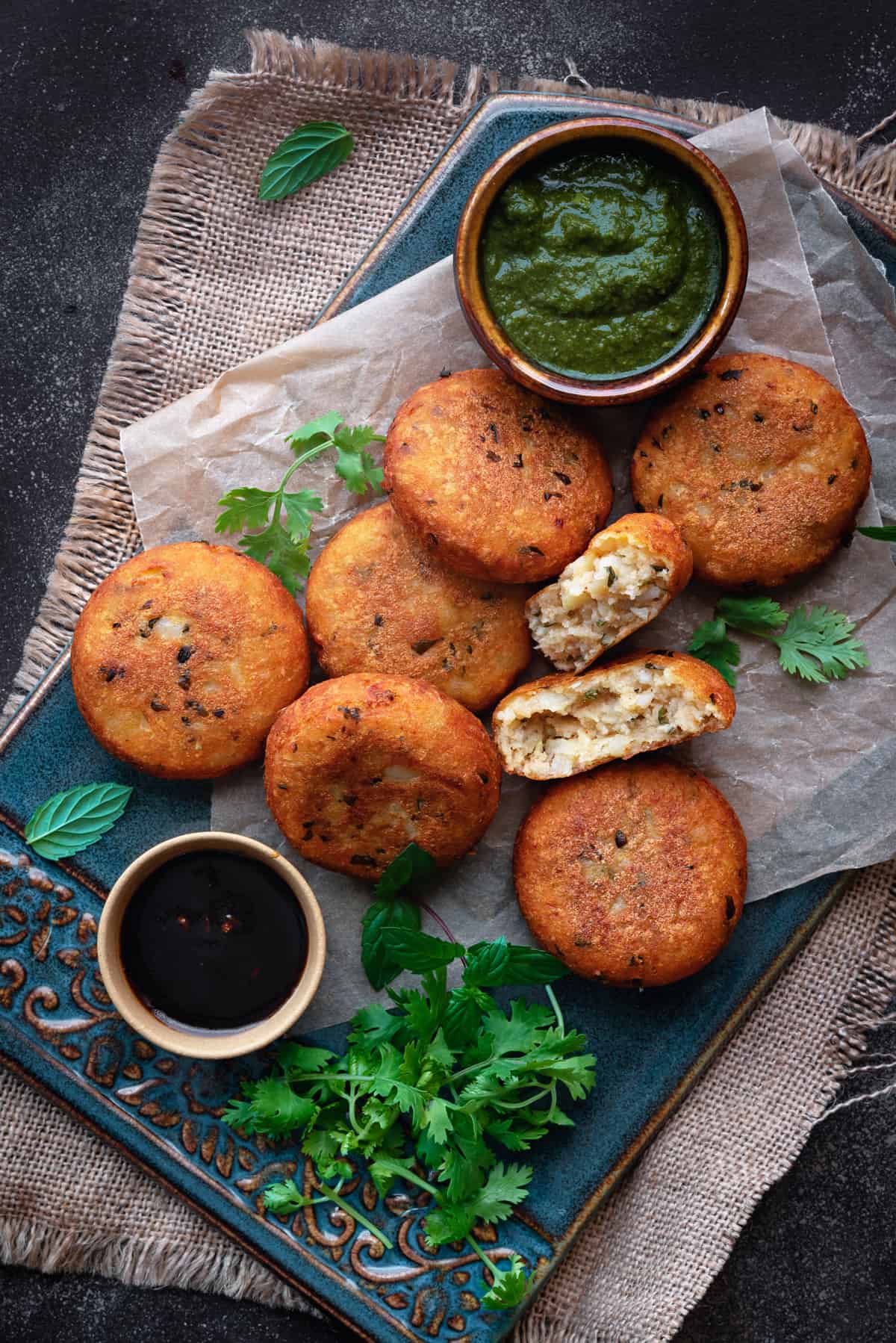 Crispy aloo tikki with one patty open served with chutney on blue ceramic tray.