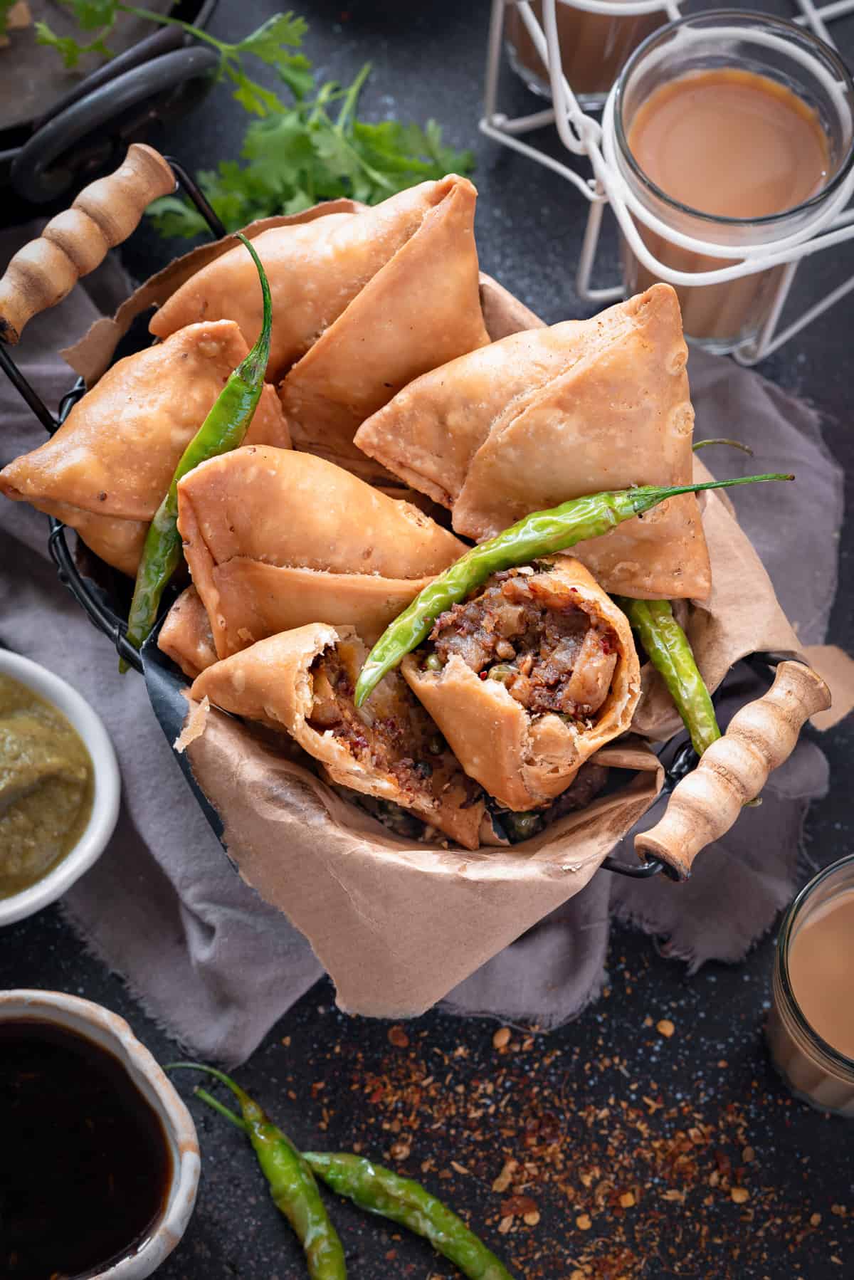 Flaky samosas in basket with one samosa cut open to show the filling within.