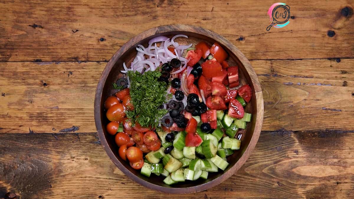 Diced cucumber, tomato, onion, olives, dill, olive oil, vinegar, salt and pepper added in wooden bowl.