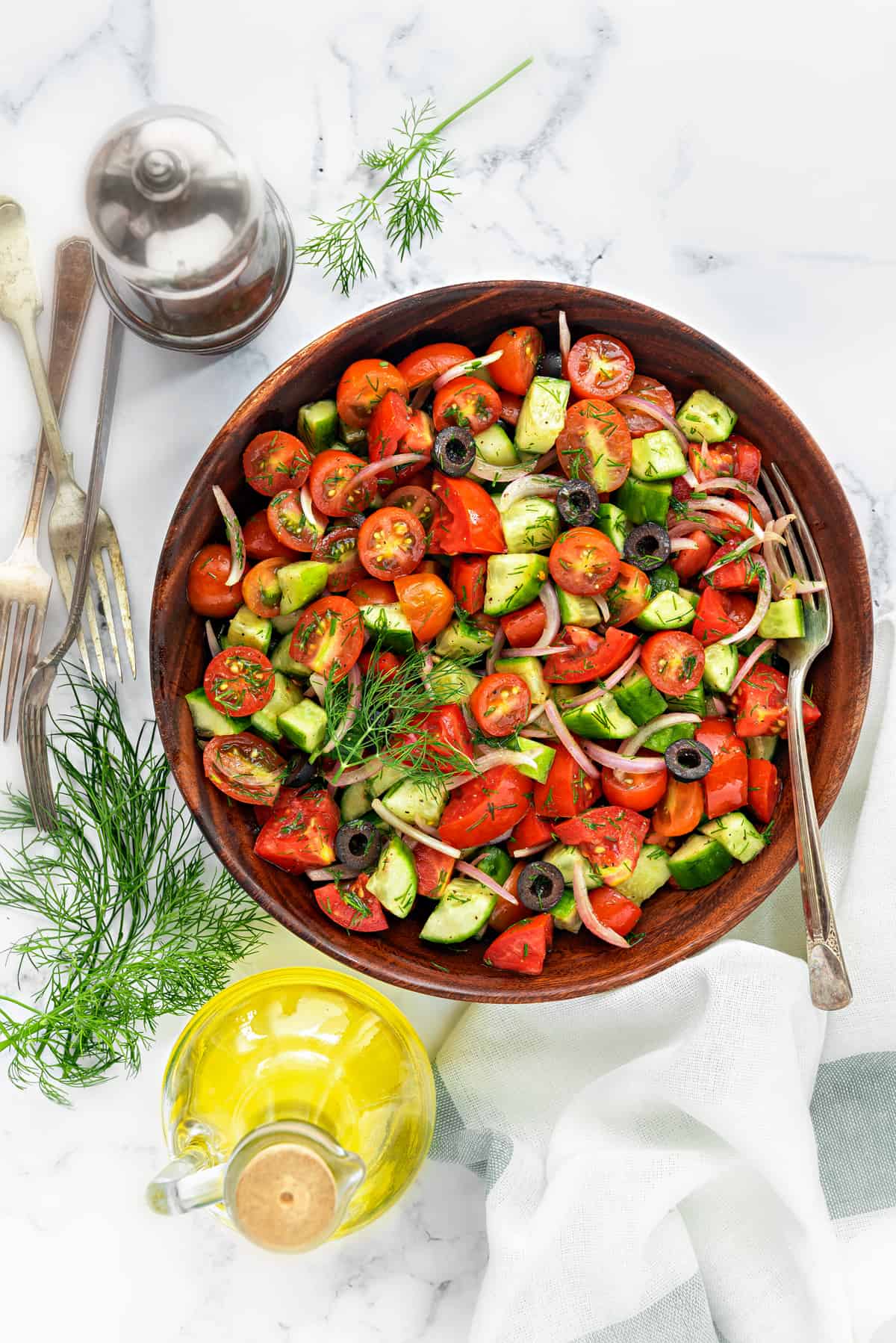 Healthy onion cucumber tomato salad in wooden bowl with fork in it and oil bottle on side.