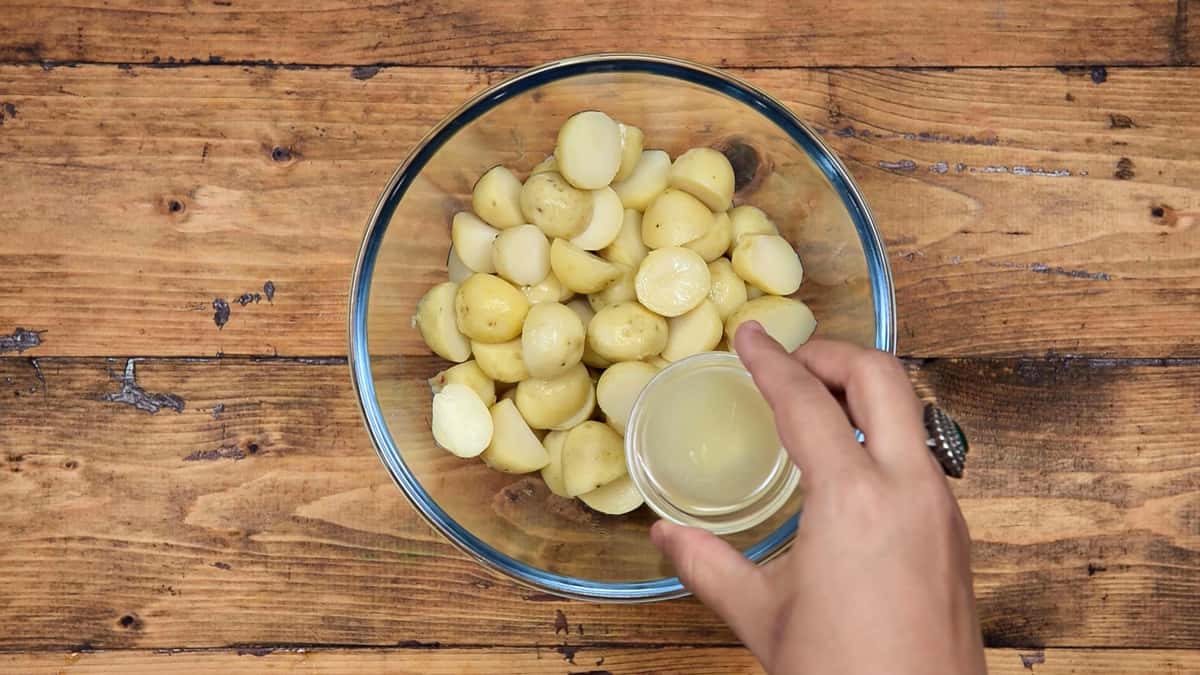Adding lemon juice to boiled, peeled and halved baby potatoes in bowl.