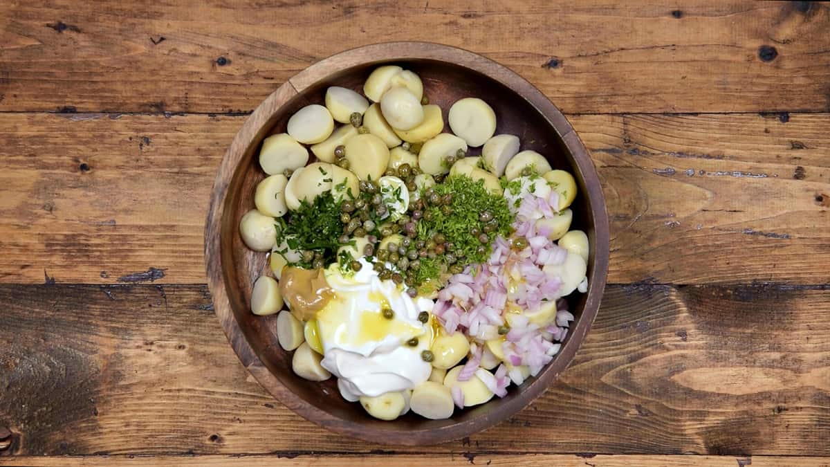 Remaining salad ingredients added to the potatoes in wooden salad bowl.