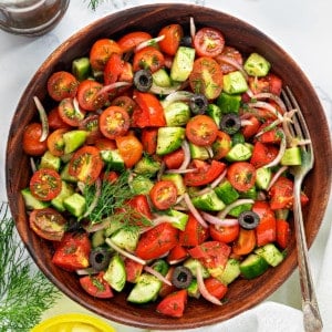 Healthy onion cucumber tomato salad in wooden bowl with fork in it.