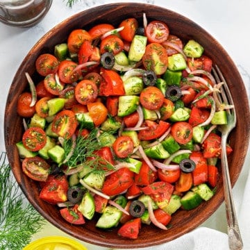 Healthy onion cucumber tomato salad in wooden bowl with fork in it.