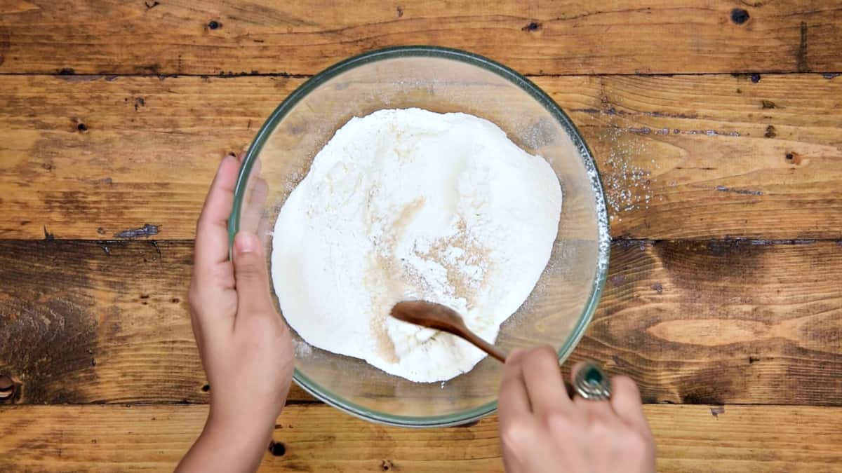 Mixing sugar into the sifted flour mix using wooden spoon.