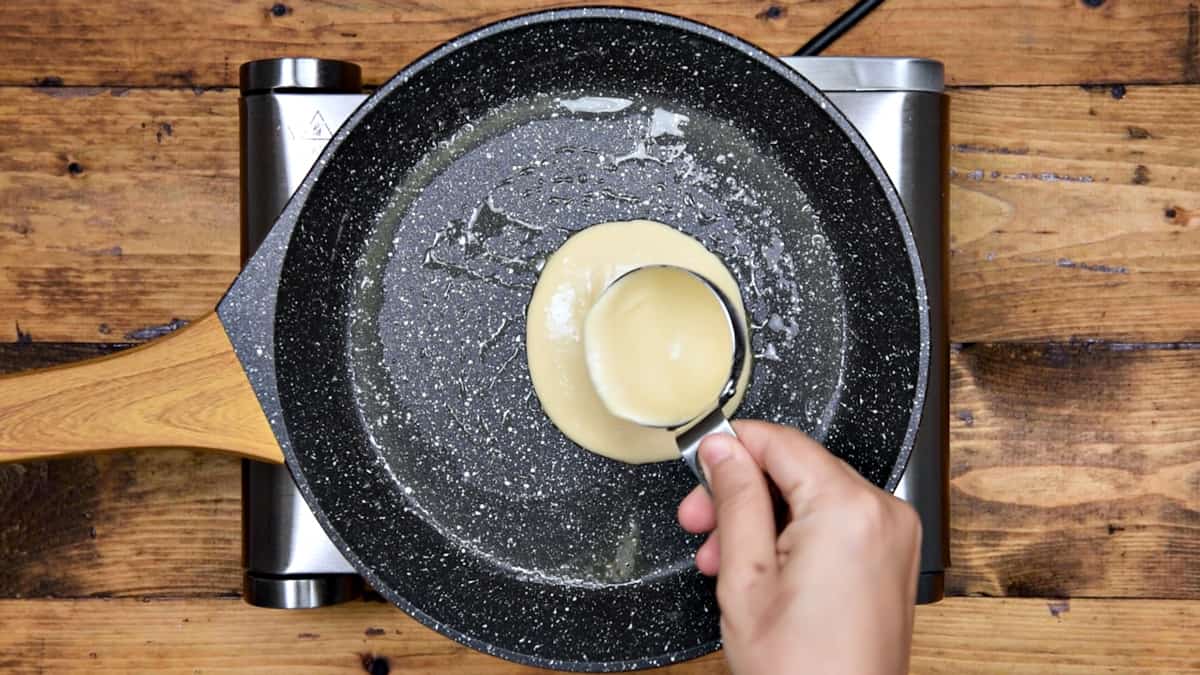 Pouring ¼ cup of pancake batter onto a greased hot pan.