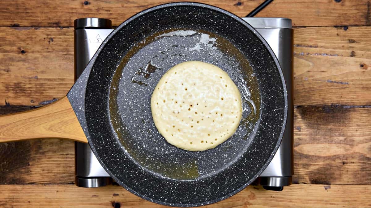 Pancake cooking in pan showing bubbles appeared on the top and is ready to flip.