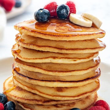 Stack of homemade Fluffy Pancakes topped with berries, banana slices and maple syrup.