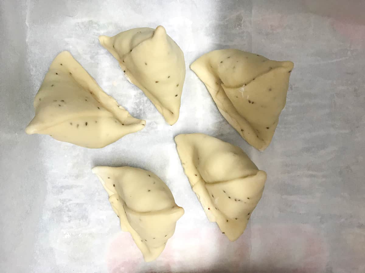 Image showing 5 frozen aloo samosa placed on parchment paper.