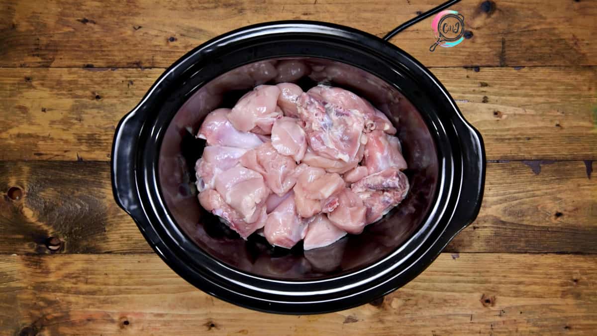 Chicken pieces added in slow cooker pot.