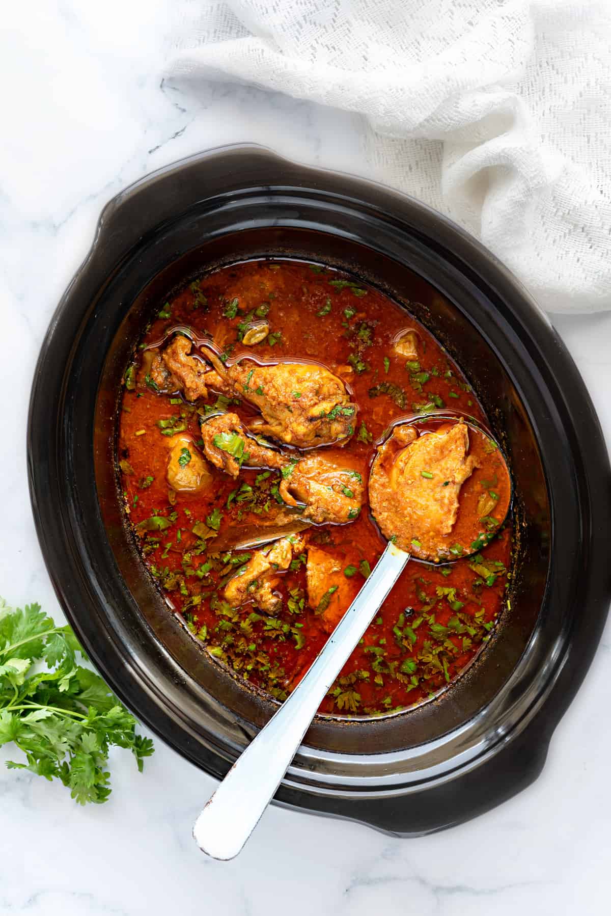 Chicken Curry masala gravy in slow cooker pot with a ladle holding chicken piece.