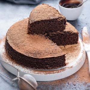 Eggless chocolate cake on white plate with one cut slice on the top of the cake.