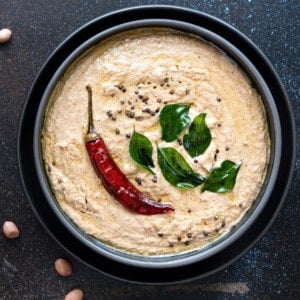 Close up shot of Peanut chutney in black bowl with few groundnut seeds spread around.