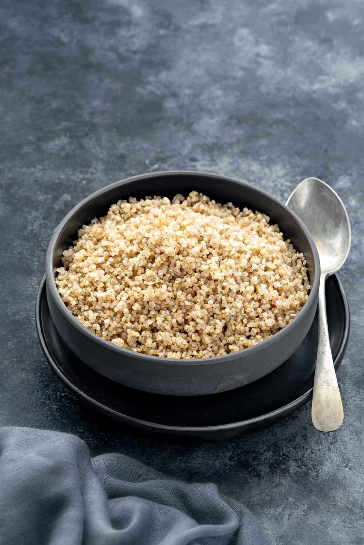 Angled shot of Instant pot quinoa served in black bowl with spoon on side.